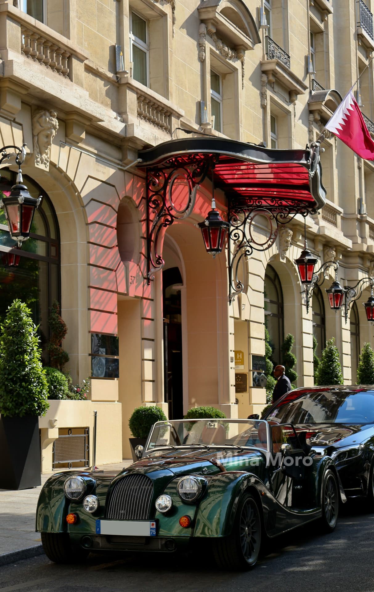 A green vintage roadster parked outside a Parisian hotel entrance with red lanterns